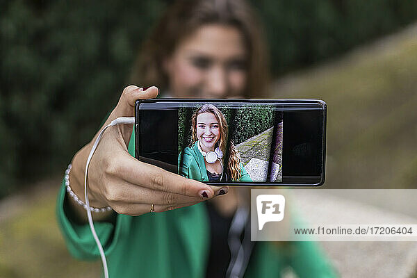 Frau zeigt mit Smartphone aufgenommenes Selfie im Freien