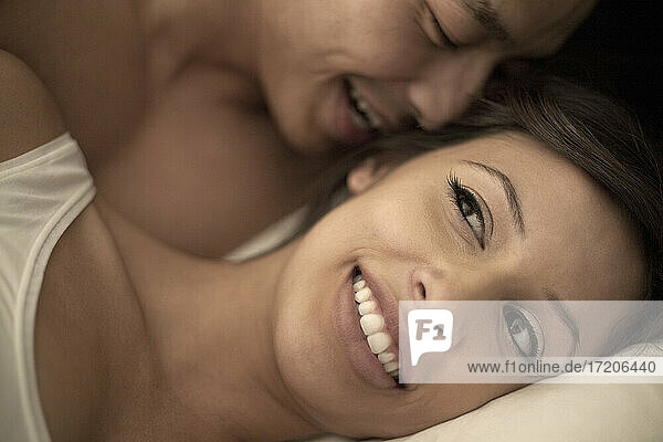 Boyfriend whispering in smiling girlfriend's ear at bedroom