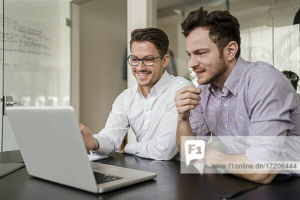 Male entrepreneur working on laptop with colleague at office
