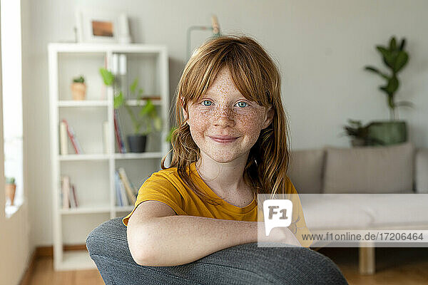 Smiling redhead girl with blue eyes sitting on chair at home