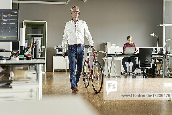 Älterer Geschäftsmann mit Fahrrad in einem Großraumbüro