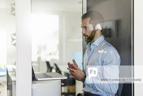 Männlicher Berufstätiger  der einen Videogespräch über einen Laptop in einer Telefonzelle im Büro führt