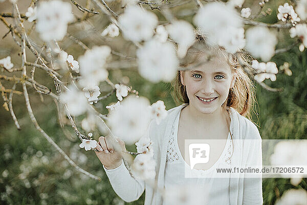 Nettes Mädchen lächelt  während es einen Zweig einer Mandelbaumblüte im Frühling hält
