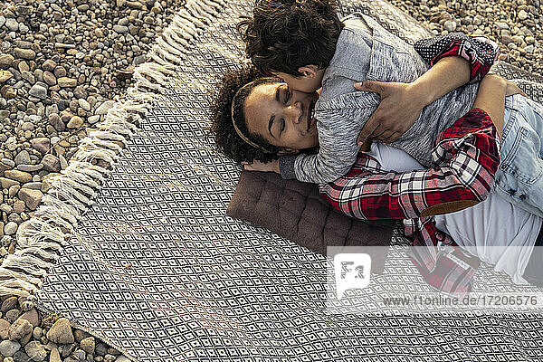 Frau  die einen Jungen umarmt  während sie auf einer Decke über einem Kieselstein liegt