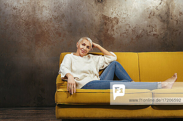 Beautiful senior woman sitting on sofa against wall
