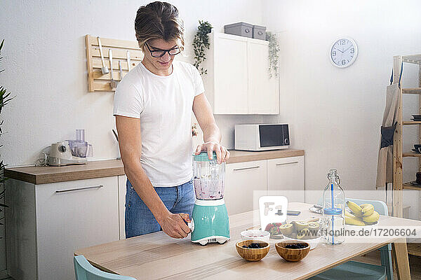 Young man preparing smoothie in kitchen