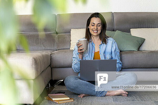 Smiling woman having coffee while using laptop in living room