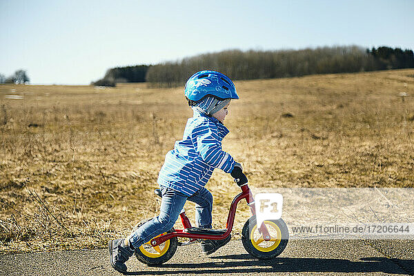 Junge mit Fahrradhelm auf dem Balance-Bike auf der Straße