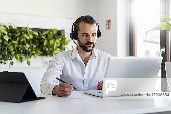 Unternehmer mit Kopfhörern bei der Arbeit am Laptop im Büro