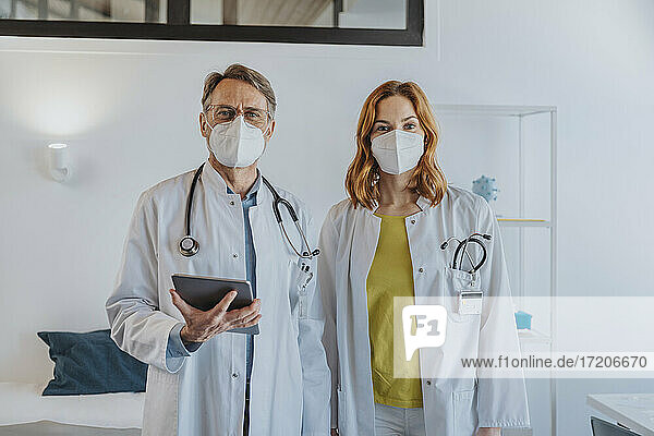 Männlicher Arzt mit digitalem Tablet  der neben einem Mitarbeiter in einer Klinik steht