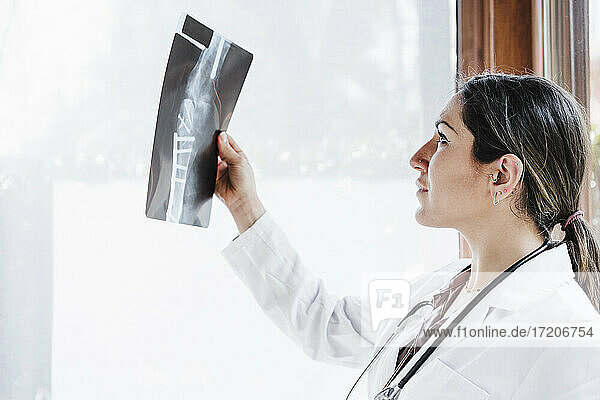 Weibliches medizinisches Fachpersonal  das ein Röntgenbild eines Knochens durch ein Fenster betrachtet
