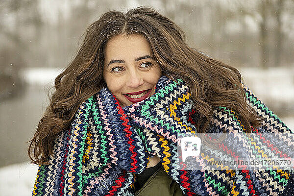Smiling woman wrapped in multi colored blanket while looking away during winter