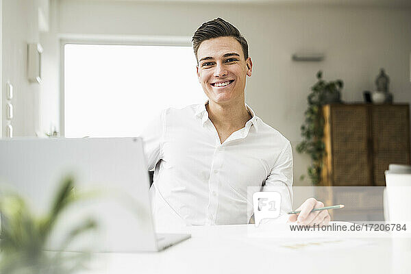 Smiling young man with laptop sitting at desk