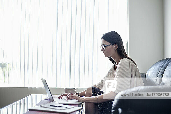 Young woman wearing eyeglasses working on laptop while sitting at home