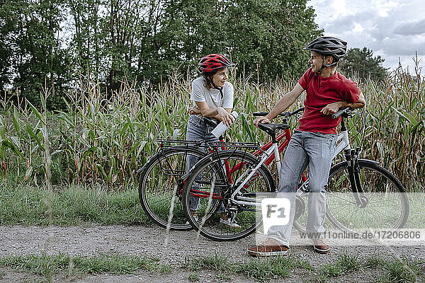 Father and daughter talking while leaning on bicycle at agricultural field