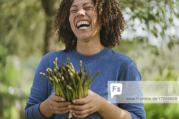 Lachende Frau mit frischem grünen Spargel im Permakultur-Garten