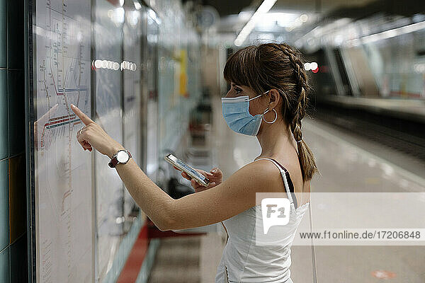 Frau mit Gesichtsschutz  die auf dem Bahnsteig einen Plan des Zuges während einer Pandemie betrachtet