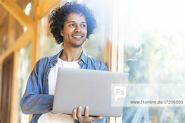Junger Mann mit Laptop schaut durch ein Fenster  während er im Vorgarten steht