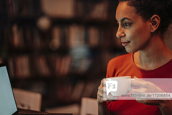 Lächelnde Frau  die Kaffee trinkt und einen Laptop benutzt  während sie im Cafe sitzt