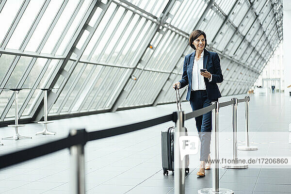 Mature businesswoman with suitcase walking in corridor