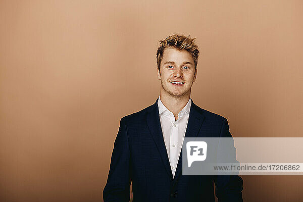 Handsome businessman standing against brown background