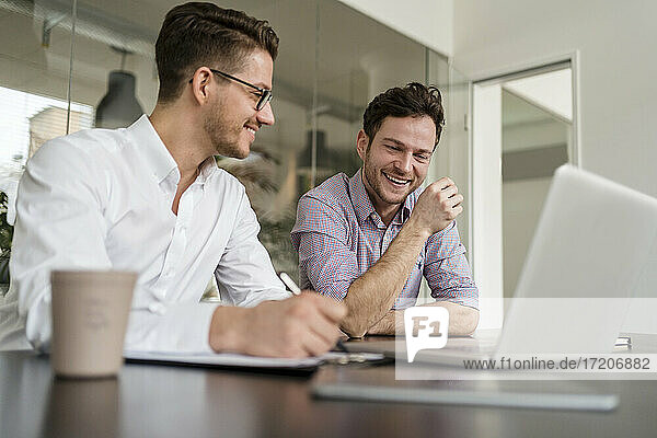 Business people smiling while discussing over laptop at office