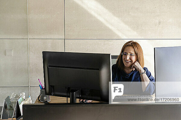 Lächelnde Geschäftsfrau  die an einem Computer arbeitet  während sie am Schreibtisch in einer Kabine sitzt