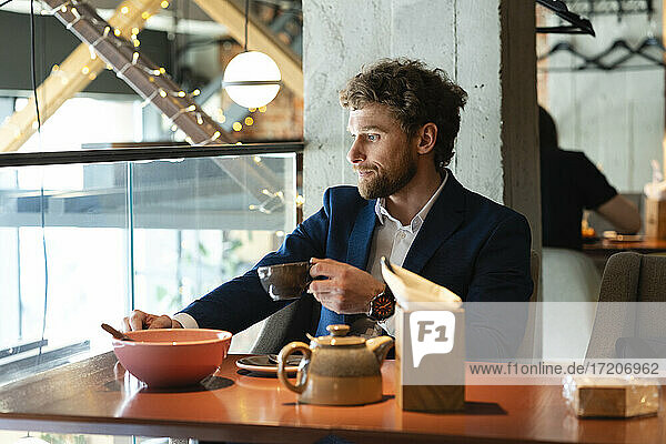 Thoughtful businessman holding tea cup while sitting at cafe