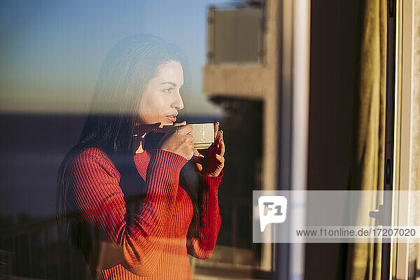 Frau trinkt Kaffee und schaut durch das Fenster zu Hause
