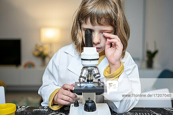 Mädchen im Laborkittel schaut zu Hause durch ein Mikroskop