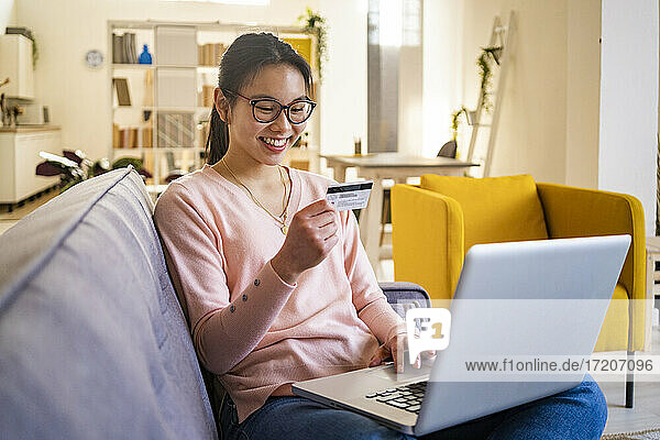 Glückliche Frau sitzt mit Kreditkarte und Laptop zu Hause