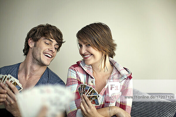 Lächelndes Paar spielt mit einem Freund Karten  während es zu Hause sitzt