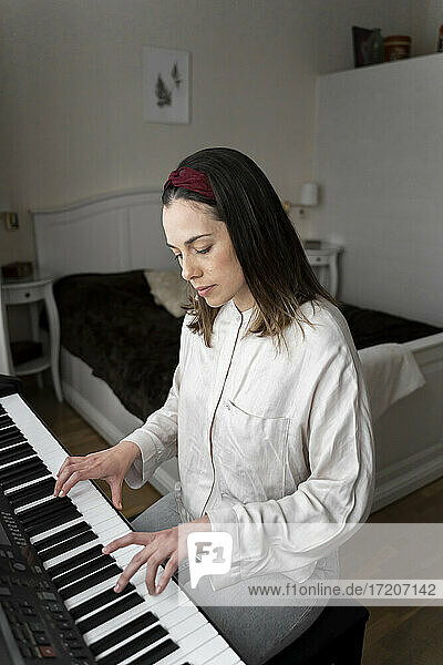 Woman playing piano while sitting in bedroom