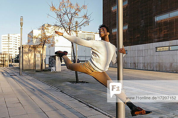 Flexibler männlicher Tänzer klettert beim Tanzen in der Stadt auf einen Laternenpfahl