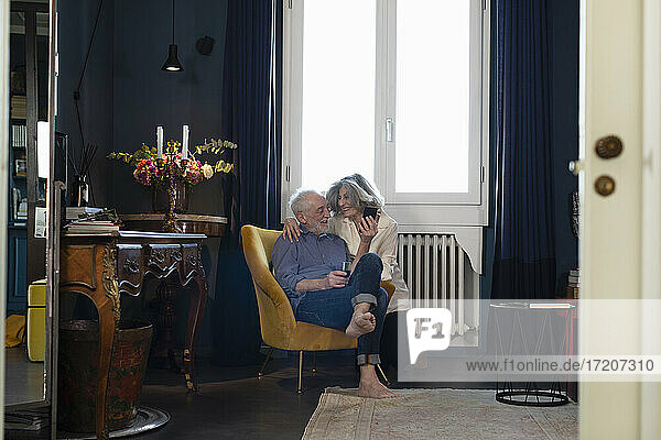 Lächelndes älteres Ehepaar  das zu Hause sitzend ein Mobiltelefon benutzt