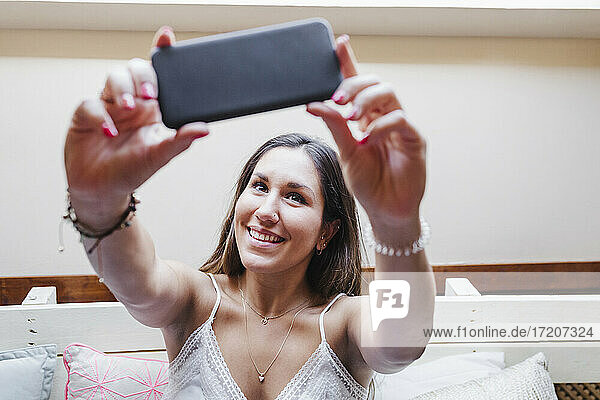 Lächelnde Frau nimmt Selfie durch Handy im Schlafzimmer