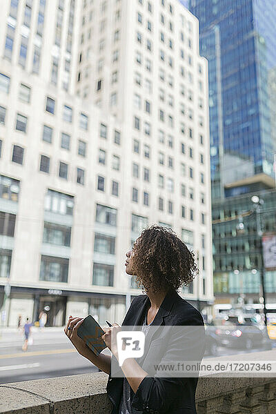 Nachdenkliche Afro-Geschäftsfrau mit Tagebuch  die sich Bürogebäude in der Stadt ansieht