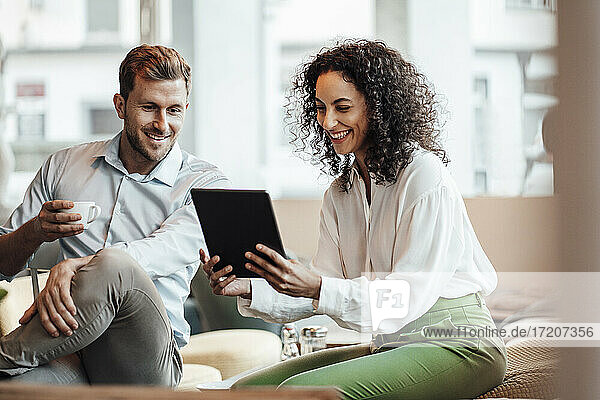 Lächelnde Geschäftsfrau  die ein digitales Tablet benutzt  während sie mit einem Kollegen in einem Cafe sitzt