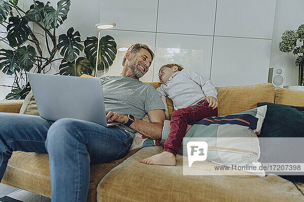 Happy father with laptop and son on sofa in living room