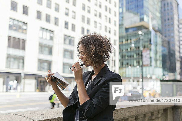 Female entrepreneur reading diary while standing near office buildings in city
