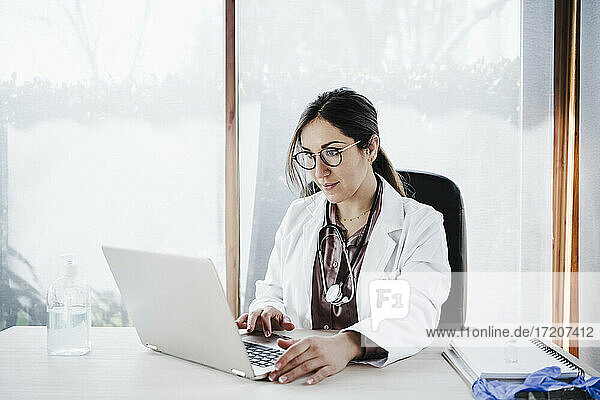 Weibliches medizinisches Fachwissen bei der Benutzung eines Laptops  während sie im Krankenhaus am Fenster sitzt