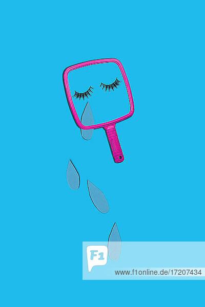 Hand mirror with eyelashes and teardrops on blue background