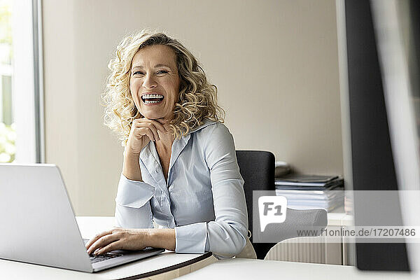 Lachende Geschäftsfrau mit Laptop im Büro sitzend
