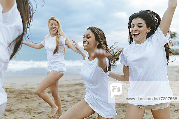 Carefree female friends with arms outstretched enjoying at beach during vacations