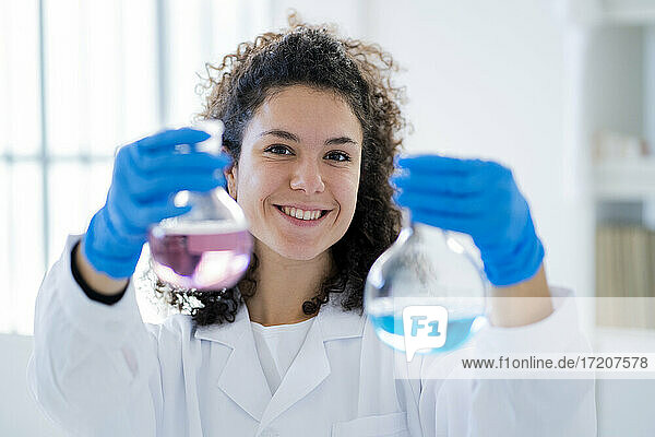 Lächelnde Wissenschaftlerin  die eine chemische Lösung in einem Becherglas in einer Klinik testet