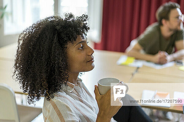 Junge afroamerikanische Unternehmerin hält Becher während einer Besprechung im Büro