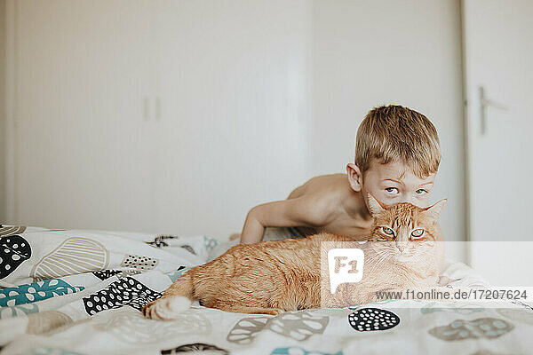 Junge küsst Ingwerkatze auf dem Bett zu Hause