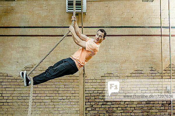 Männlicher Mann hängt an einem Seil an einer Mauer im Fitnessstudio