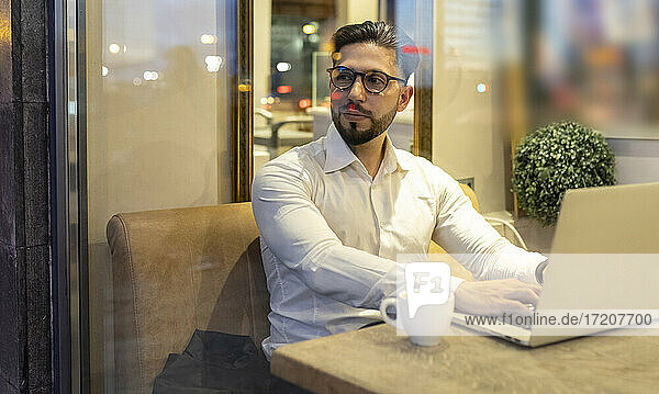 Männlicher Unternehmer schaut weg  während er einen Laptop in einem Café benutzt