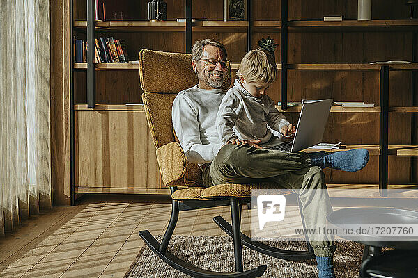 Boy using laptop while sitting with father on chair